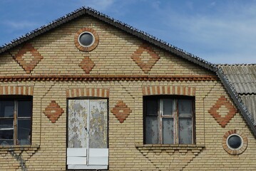 Obraz premium brown brick attic of a rural house with windows and a door on a blue sky background