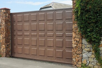 one large brown gate and part of a stone fence in green vegetation on the street
