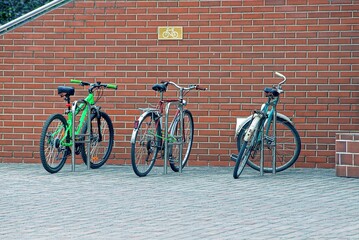 Naklejka premium three bicycles are parked on the street against a brown brick wall