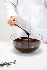 Closeup female chef stirring and pouring dark melted chocolate isolated on white background. Chocolatier make organic couverture high-quality hand-crafted chocolate. Candymaking, confectionery concept
