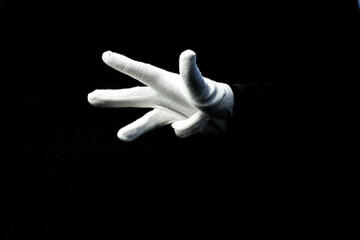 A hand wearing white glove on black background showing number 4 sign