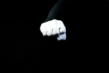 A hand wearing white glove on black background showing a fist