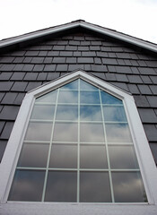Large window with cloud reflections surrounded by white trim and gray shingles