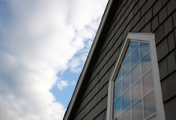 Large window with cloud reflections surrounded by white trim and gray shingles