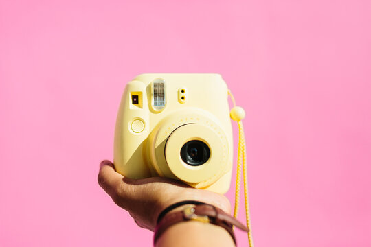A hand holding out a yellow instax polaroid camera.