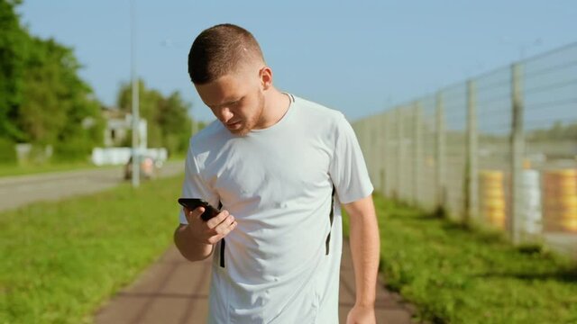 At sunlight man runner stopped checks mail use phone read good news and running outdoors on street. Young face. Sporty athletic social media internet. Slow motion