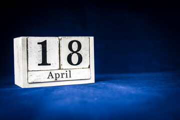 April 18th, Eighteenth of April, Day 18 of month April - rustic wooden white calendar blocks on dark blue background with empty space for text.