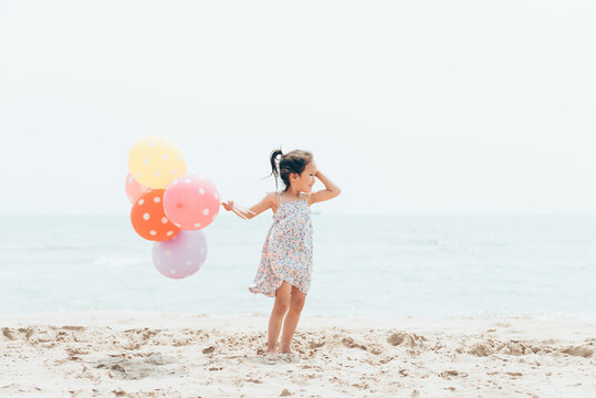 Cute toddler girl holding balloons on the seaside