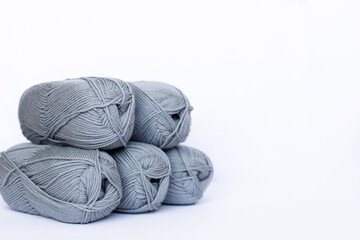 Many gray balls of thread on a white background. The threads and knitting needles lie on the background. We knit as a gift. Home crafts. Knitting hobby