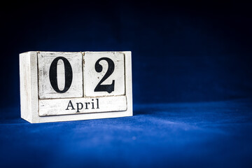 April 2nd, Second of April, Day 2 of month April - rustic wooden white calendar blocks on dark blue background with empty space for text.