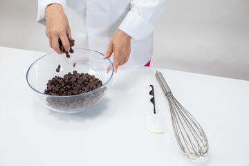Closeup female chef pours dark chocolate drops chips morsels callets isolated on white background. Confectioner preparing hand-crafted chocolate. Making candy, pastry production, dessert concept