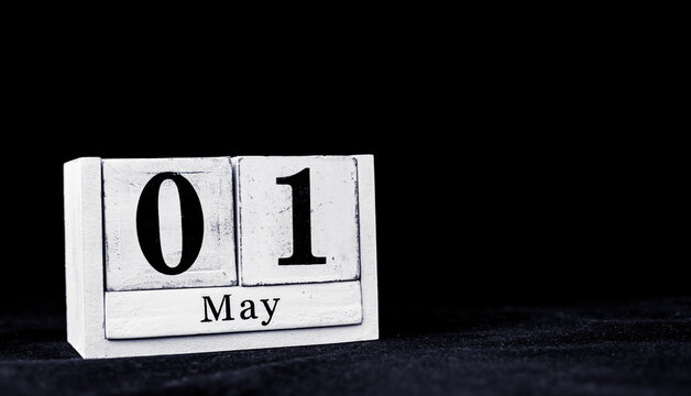May 1st, First of May, Day 1 of month May - vintage wooden white calendar blocks on black background with empty space for text