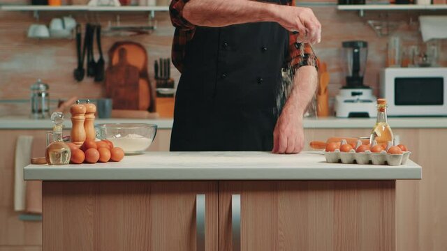 Experienced chef baker using wheat flour spreading it for food preparation. Retired senior man with bonete and apron sprinkling sieving sifting ingredients by hand baking homemade pizza and bread