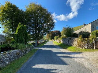 Country road, as it runs through Litton, with dry stone walls, old trees, and cottages, on a late summers day in, Littondale, Skipton, UK