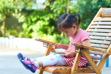 little asian girl sitting in the chair playing tablet