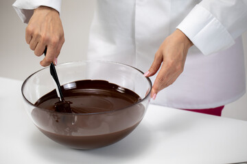 Close up mixing and stirring dark melted chocolate isolated on white background. Chocolatier make organic bitter unsweetened hand-crafted chocolate. Candy making, pastry production, dessert concept