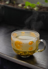 Glass cup of tea, hot drink steam on black wooden background