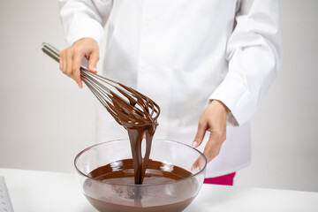 Closeup female chef stirring and pouring dark melted chocolate with whisk isolated on white...