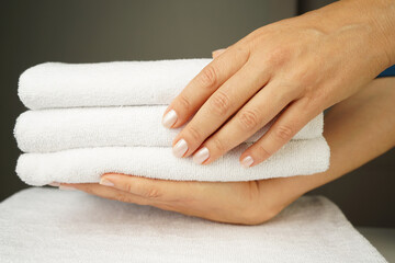 woman with beautiful hands with good manicure holds a neatly folded stack of white terry towels indoors