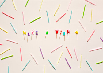 Colourful letter shaped birthday candles spell the words Make a wish on pale peach background