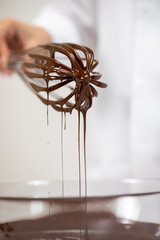 Close up sweet tasty dark melted chocolate on whisk isolated on white background. Chocolatier making premium hand-crafted chocolate. Preparing pralines, chocolate candy or truffles concept
