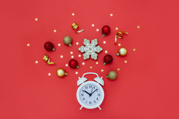 Alarm clock surrounded by Christmas decor on red background. New Year concept. Layout, top view.