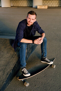 Handsome man smiling at camera with legs on longboard