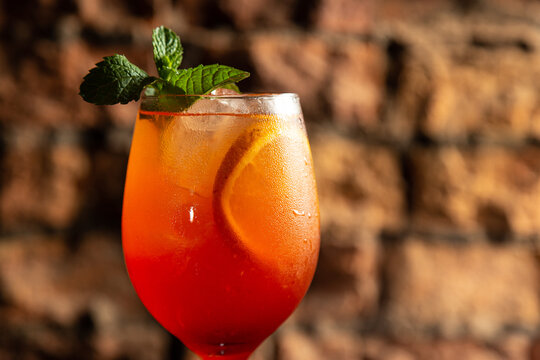 Aperol spritz cocktail in big wine glass with bloody oranges decorated with peppermint, summer Italian fresh alcohol cold drink. Bricks bar wall background, selective focus