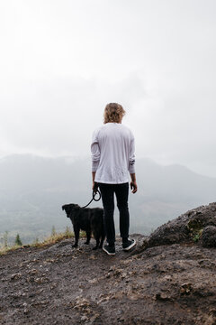 Young man and his dog looking out over a foggy forest on a rainy day