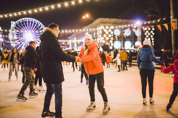 Beautiful Couple Ice Skating In City Centre. Young couple skating at a public ice skating rink outdoors. Theme ice skating rink and loving couple. Amazing winter holiday. Saint Valentine's Day