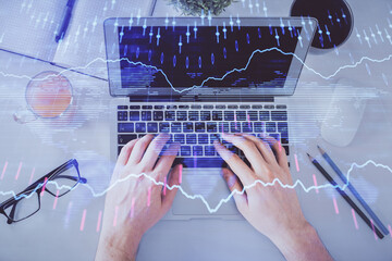 Double exposure of man's hands typing over laptop keyboard and forex chart hologram drawing. Top view. Financial markets concept.