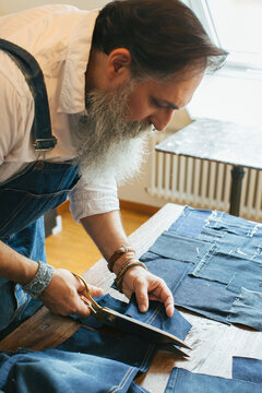 Closeup of Cool Senior Man with Grey Hipster Beard Cutting Denim Material