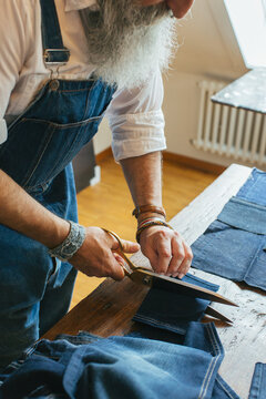 Closeup of Fashionable Senior Man Cutting Denim Fabric on Living Room Table