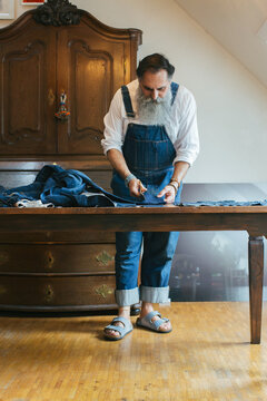 Indoor Portrait of Fashionable Senior Male Tailor Cutting Denim Fabric