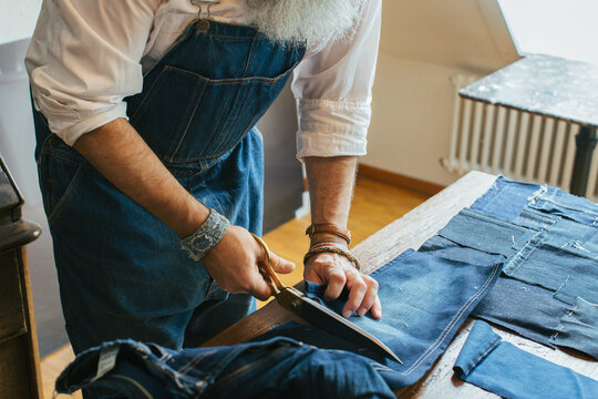 Closeup of Cool Senior Man Cutting Denim Fabric on Living Room Table