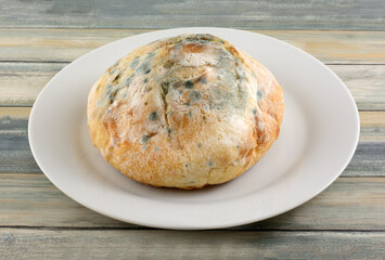 Mold growing on round loaf of French boule bread on white plate on table