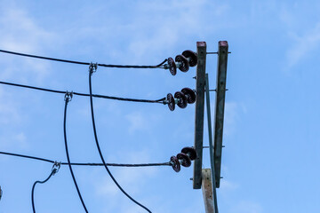 wires with electrical insulator mounted on an iron pole against a blue sky