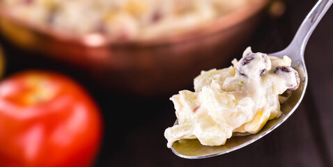 silver spoon with homemade mayonnaise in focus, typical food of celebrations in Brazil, made with vegetables, potatoes, fruits, toamtes and eggs