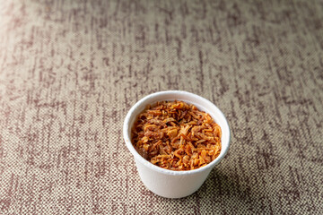 dry and caramelized onions folded in a paper cup stands on a gray table