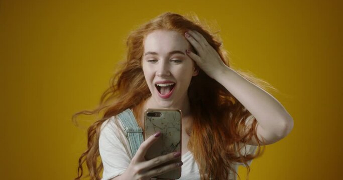 Cute authentic redhead caucasian girl using her smartphone, scrolling social media and getting amazed with hair on wind 4k footage