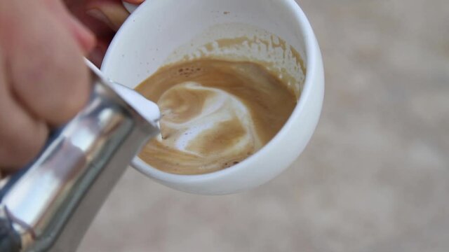 The making of a cappuccino. Male hands doing latte art with a pitcher. Pouring milk into espresso. Mixing milk and milk foam with coffee.. Serving coffee with milk. No body.