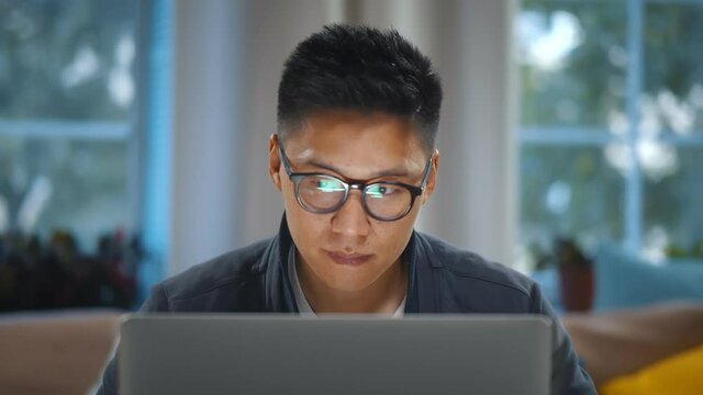 Close up of young asian man in glasses working on laptop at home office