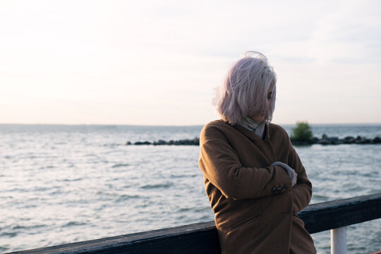 Pink-haired woman in coat cold on pier