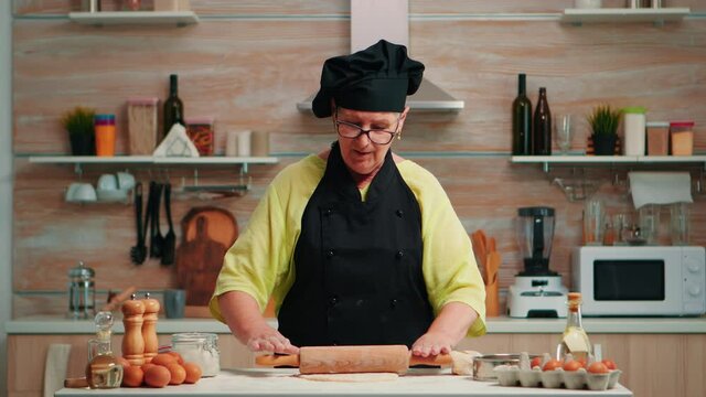 Baker woman rolling dough at home infront of video camera explaining recipe step by step. Retired blogger chef influencer using internet technology communicating on social media with digital equipment