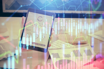 Double exposure of man's hands holding and using a digital device and forex graph drawing. Financial market concept.