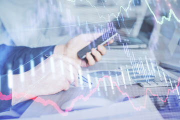 Double exposure of man's hands holding and using a digital device and forex graph drawing. Financial market concept.