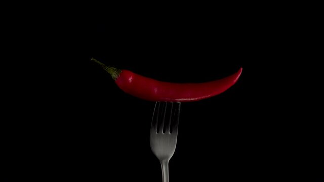 Hot red chili pepper on the fork rotates on a black background. Spicy food concept. Close up 4K