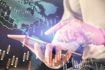 Double exposure of man's hands holding and using a digital device and forex graph drawing. Financial market concept.