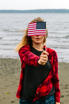 Young Woman On Ocean Beach Holding Mini American Flag In Front O