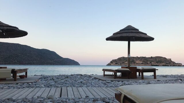 Pebbled beach with sunshades and sun loungers and sea at sunset